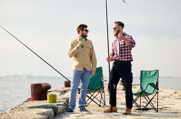 happy friends with fishing rods and beer on pier