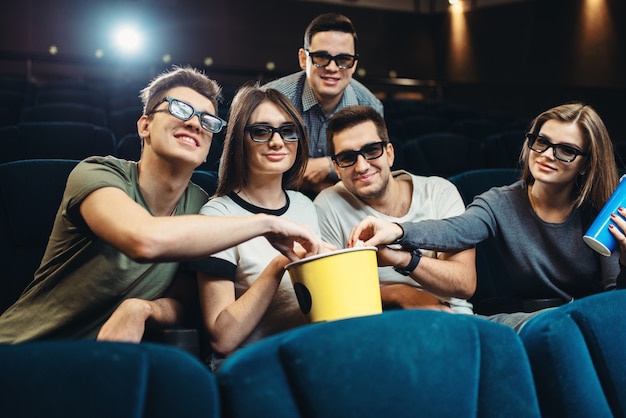 Happy friends with popcorn and drinks watching movie in cinema. Entertainment business