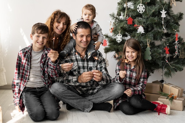 Happy full family and three children at home with Christmas gifts sitting at home on the floor in the morning under a Christmas tree in winter