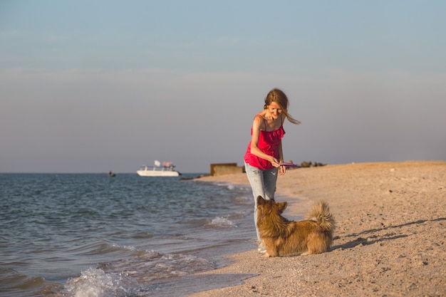 Happy fun weekend by the sea - girl playing at the frisbee with a dog on the beach. Summer