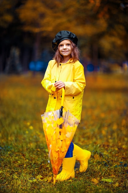 Ragazza felice bambino divertente con ombrello multicolore in stivali di gomma al parco d'autunno.
