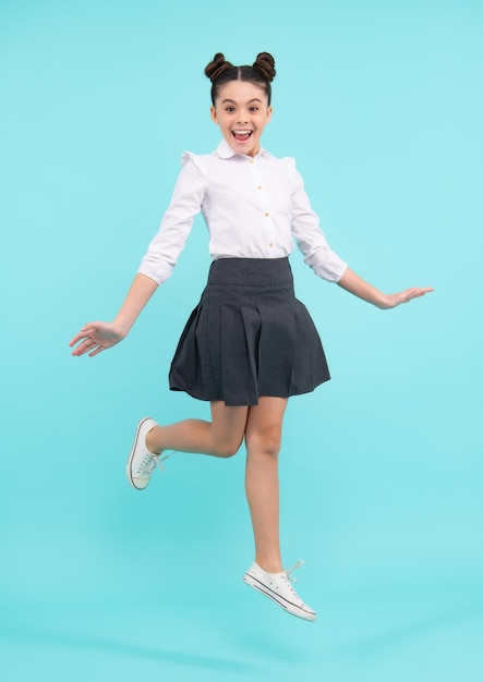 Happy funny excited jumping teenager Happy schoolgirl positive and smiling emotions of teen girl Full length jump of teenager girl on blue isolated studio wear casual skirt and shirt