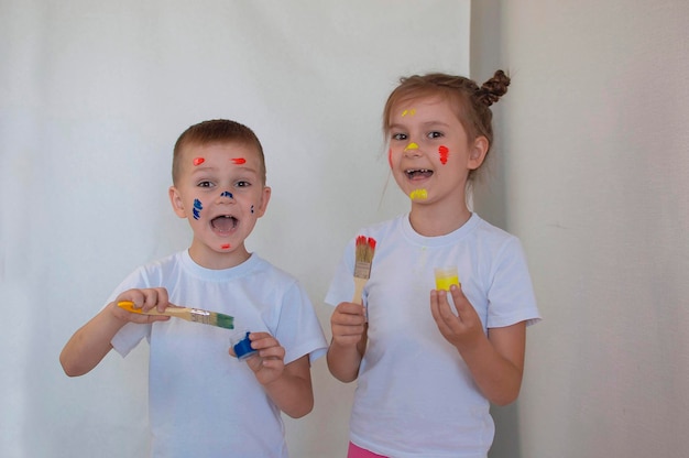 행복한 재미있는 어린 아이들은 종이에 손가락으로 즐겁게 그림을 그립니다. 아이들의 손과 얼굴은 여러 가지 빛깔의 페인트로 칠해져 있습니다.