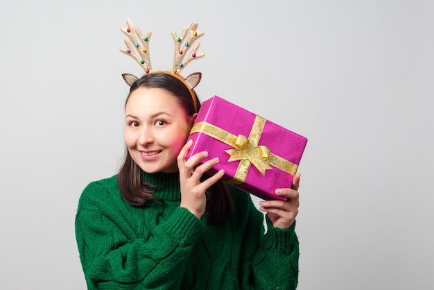 贈り物とクリスマス鹿の角を持つ幸せな面白い女性。白い背景に