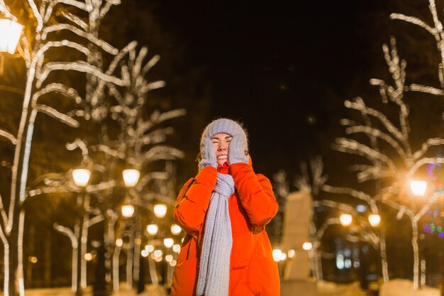 冬の服の背景の夜の街の明かりのイルミネーションと幸せな面白い若い女性。クリスマスと冬の休日のコンセプト。