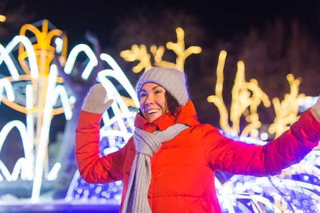 Счастливая смешная молодая женщина с зимней одеждой на фоне вечерних огней города рождество