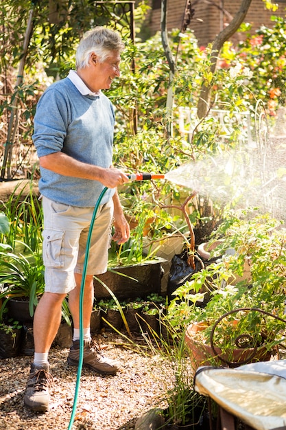 Happy gardener watering plants from hose at garden