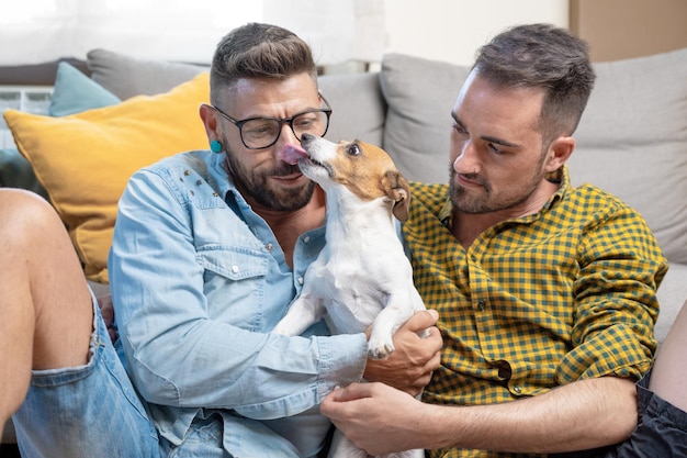 Felice coppia gay seduta sul pavimento e giocare con il cane a casa