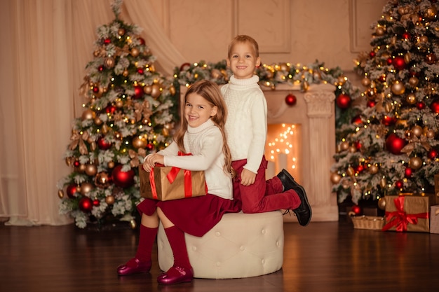 Fratello e sorella happy gemini si scambiano un regalo di capodanno a casa vicino al camino e all'albero di capodanno