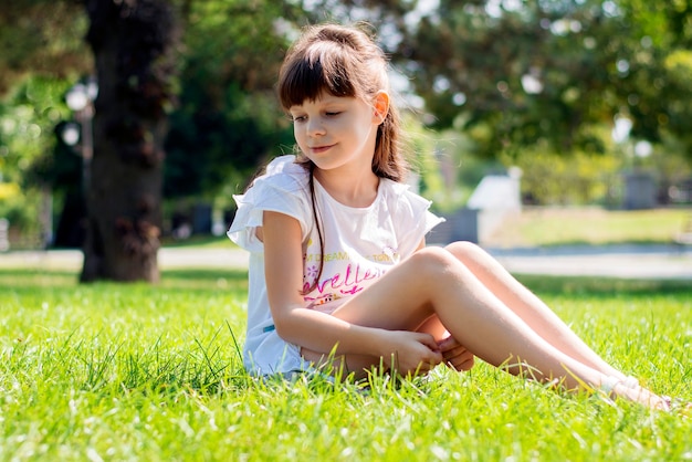 Photo happy girl of 8 years old in a white dress and long dark hair sits on a green lawn