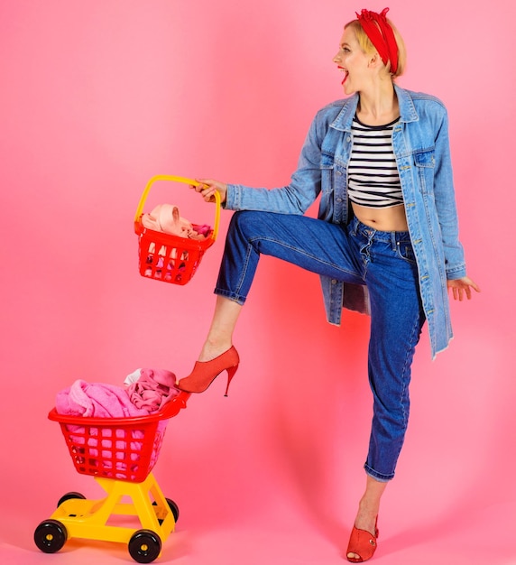 Photo happy girl after shopping smiling woman with shopping basket and shopping cart with clothes on shop