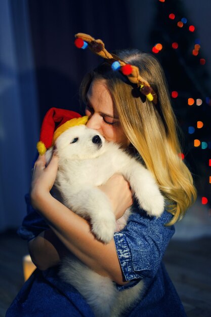 Foto ragazza felice in corna con cane husky samoiedo in decorazioni natalizie