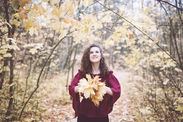 Happy girl in an atumn park throwing maple leaves