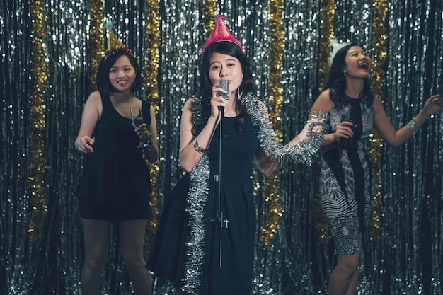 Happy girl band performing on the stage in club. young asian
ladies singing and dancing in a karaoke party at nightclub. group
of women enjoy music and alcohols in midnight lifestyle
concept.