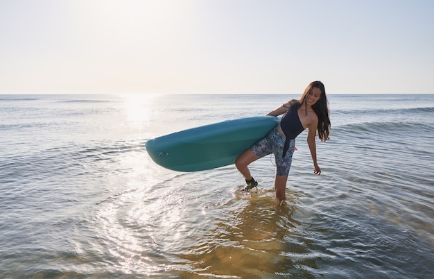 Счастливая девушка на пляже с доской для серфинга