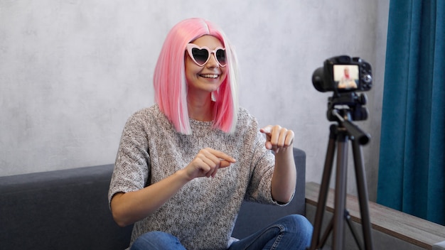 Foto blogger ragazza felice in parrucca rosa davanti alla telecamera su un treppiede. registra un video blog