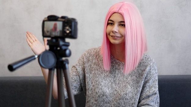 Happy girl blogger in pink wig in front of the camera on a tripod