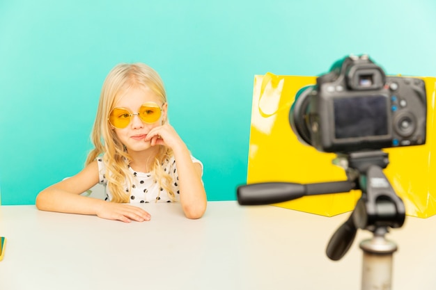 Happy girl in the blue studio speaking in front of camera for vlog. Working as blogger, recording video tutorial for Internet.