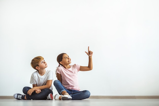 幸せな女の子と男の子が床に座って身振りで示す