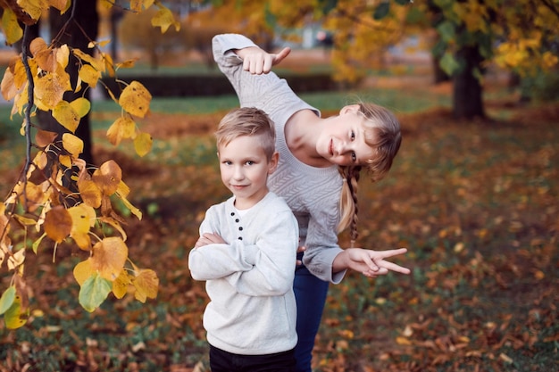 Счастливая девочка и мальчик бросают желтые осенние листья в лес