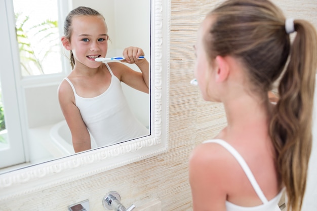 Ragazza felice che pulisce i suoi denti in bagno