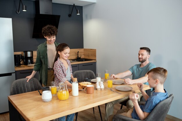 Happy girl in casualwear putting plate with homemade sandwiches on dinner table while helping mother with breakfast in the kitchen