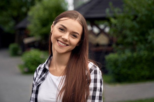 Happy girl in checkered shirt posing outdoors.