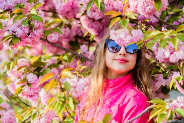 Happy girl in cherry flower Sakura tree blooming blossom smell allergy skincare Natural cosmetics for skin summer holiday Childhood beauty small girl in spring flower Enjoying summer rest