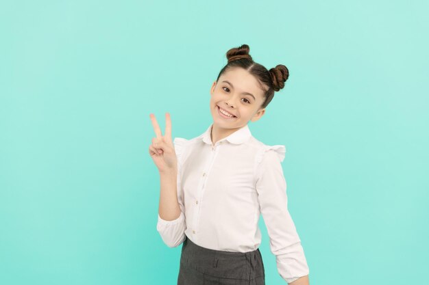 Happy girl child back to school showing V sign hand gesture blue background victory