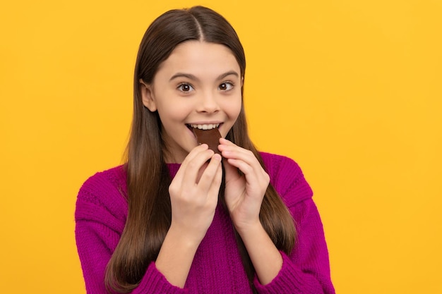 Happy girl child bite tasty chocolate slab yellow background sweettooth