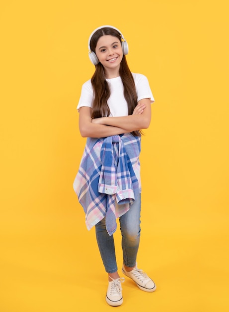 Happy girl child in casual listening to music in headphones yellow background listen