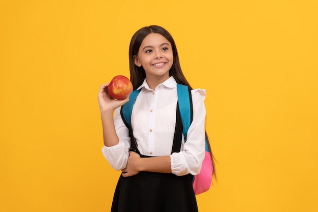 Happy girl child hold apple and school bag yellow background knowledge