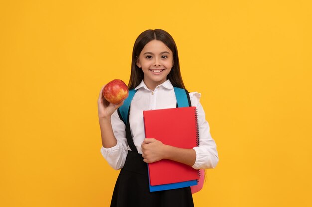 Happy girl child smile holding apple and books yellow background, school