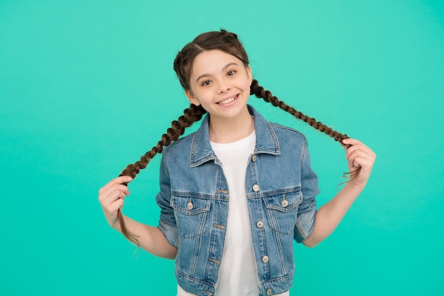 Happy girl child with beauty look hold long hair plaits in casual fashion style blue background hairstyle