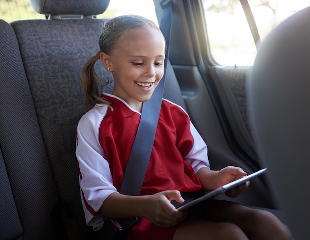 Photo happy girl child and with tablet in car smile browse online and use social media apps while buckled up female kid use digital device or after practice share winning soccer match or playing game