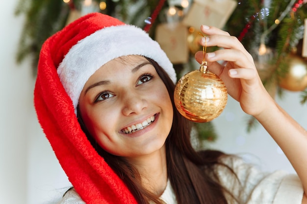 happy girl in a Christmas hat with a Christmas tree toy in her hand closeup