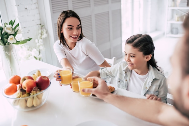 The happy girl clinks juice glasses with parents