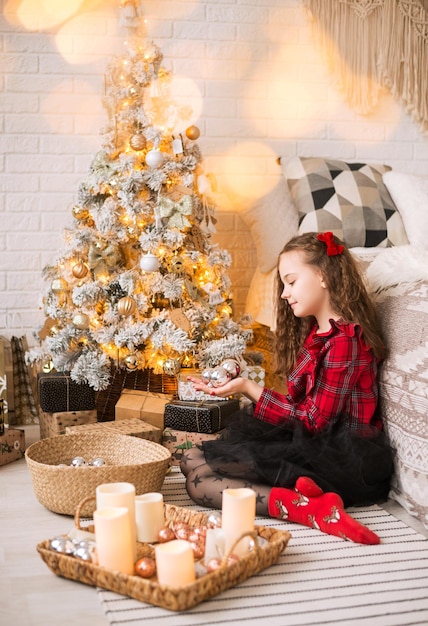 Happy girl decorate the Christmas tree. Child decorating Xmas tree at home. Kid decorate living room for Christmas.