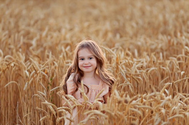 Happy girl in a dress in a wheat field at the sunset harvest