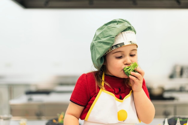 Happy girl eating broccoli in a kitchen.