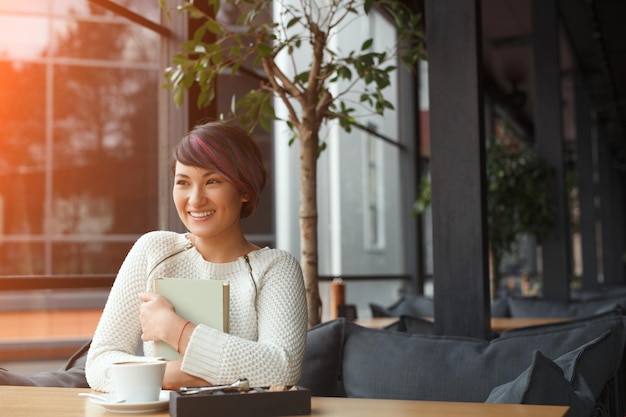 Happy girl embracing book in cafe