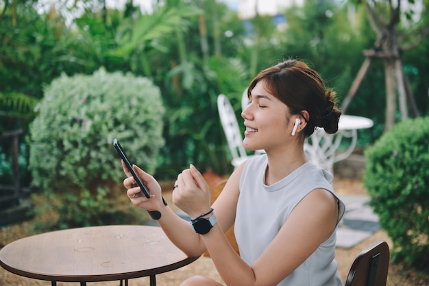 Счастливая девушка наслаждается музыкой в airpods и поет любимую песню, отдыхая в саду