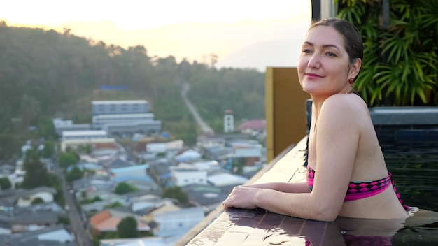 Happy girl enjoys pictorial landscape standing in hotel swimming pool in summer evening closeup