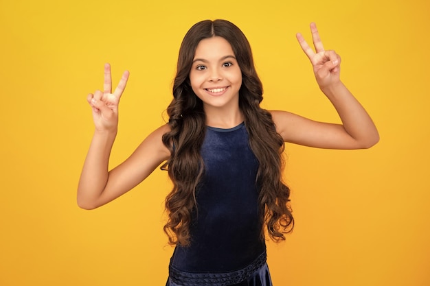 Happy girl face positive and smiling emotions Teenager child 12 13 14 years old showing fingers victory sign Number two vsign symbol isolated on yellow background