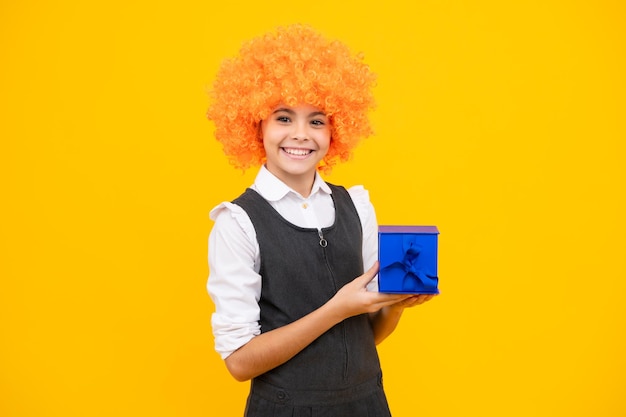 Happy girl face positive and smiling emotions teenager kid with present box teen girl giving birthday gift funny child clown in wig and gift present greeting and gifting concept