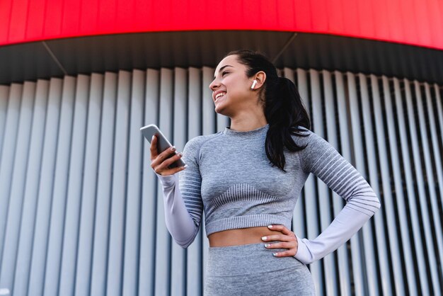 Happy girl in grey sportswear holding phone and listening to\
the music