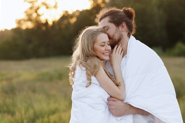 Happy girl and guy in a blanket kissing at sunset.