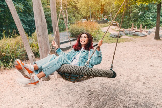 Foto la ragazza felice è caduta nell'infanzia si diverte e cavalca su un'altalena nel parco giochi per bambini l'infantilismo e la psicologia della personalità e della gioia