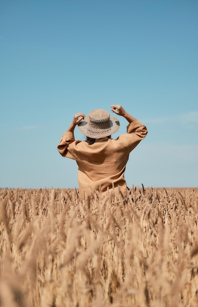 Happy girl in a hat dancing in a field on a clear blue sky background