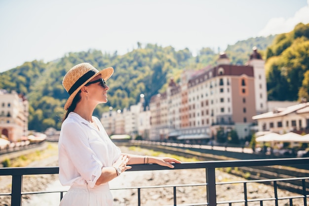 Ragazza felice al cappello sull'argine di un fiume di montagna in una città europea.